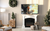 White painted fireplace with a TV mounted above, flanked by a Christmas tree on the right and a chopped wood holder on the left