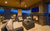 Outdoor veranda or palapa with comfy wicker-like seating and cushions facing a fireplace that's on and a mounted TV