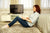 A woman sitting on a bedroom floor leaning against a bed while a smaller flat-screen TV placed atop a TV console in the background