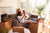 A couple sits on a couch in a sunny living room with their feet up on a moving box and opened moving boxes scattered around the floor.