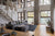 A modern living room with floor-to-ceiling windows, gray curtains, and a sculptural light fixture hanging from the ceiling over a large, gray sofa.