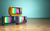 Three retro or vintage 1970s-like televisions with vertical color bars on all of the screens, with a light wood floor and teal wall as a backdrop.