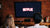 A couple facing a brick wall that has a pulldown tv mounted on it with the Netflix log on the tv screen.